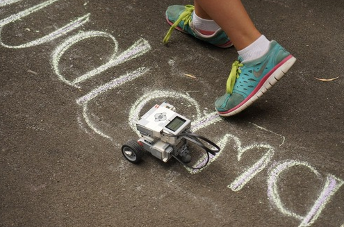 Figure 2: Detail: A robot in action, navigating the chalk-drawn map. The map was composed of region boundaries with place-names (e.g. Dharug; Dharawal) written inside them, and also pictures of geographical features (e.g. mountains). Photo: Angie Abdilla, 2014